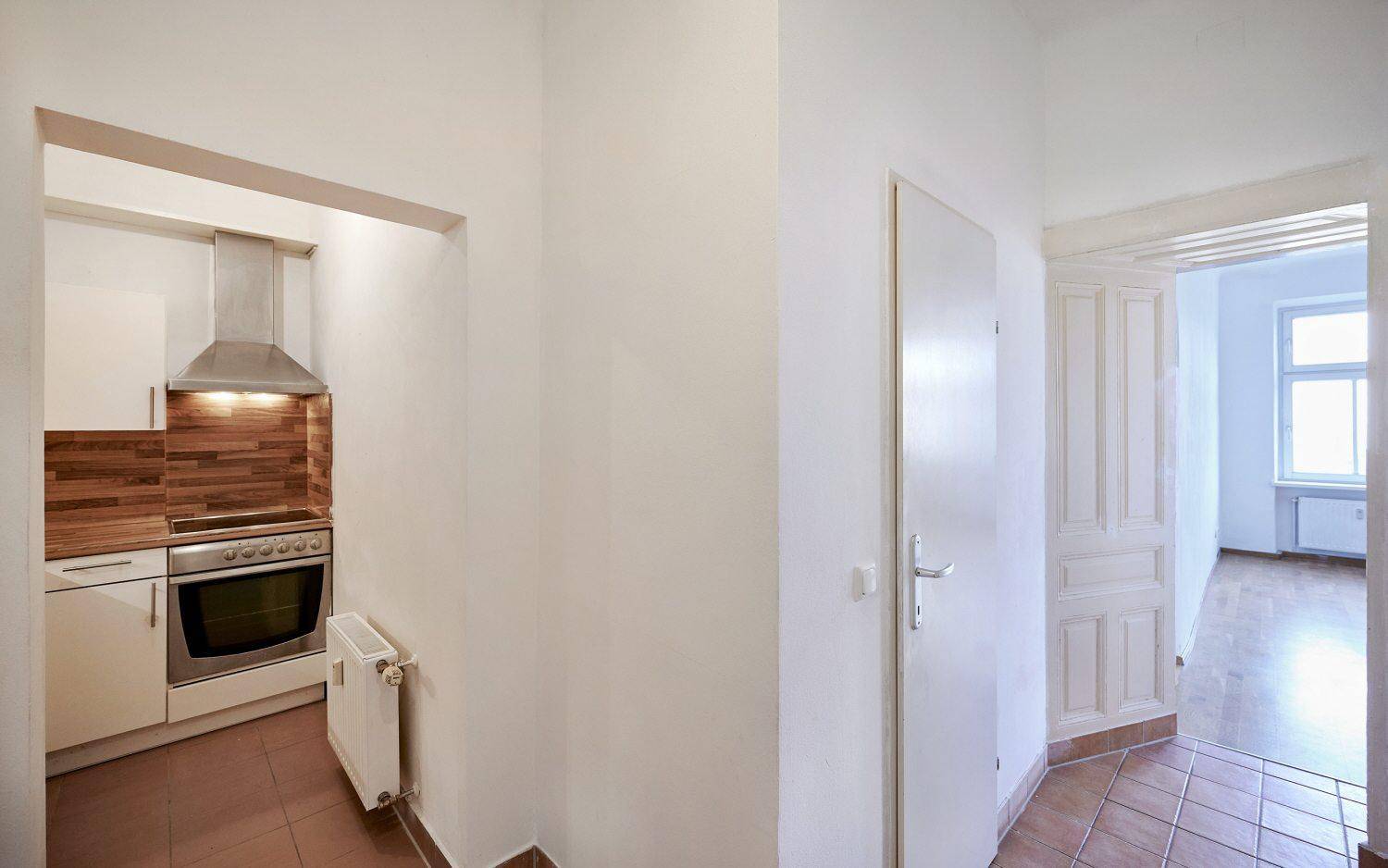 Flur mit Fliesenboden und direktem Blick in eine kompakte, moderne Küchenzeile.