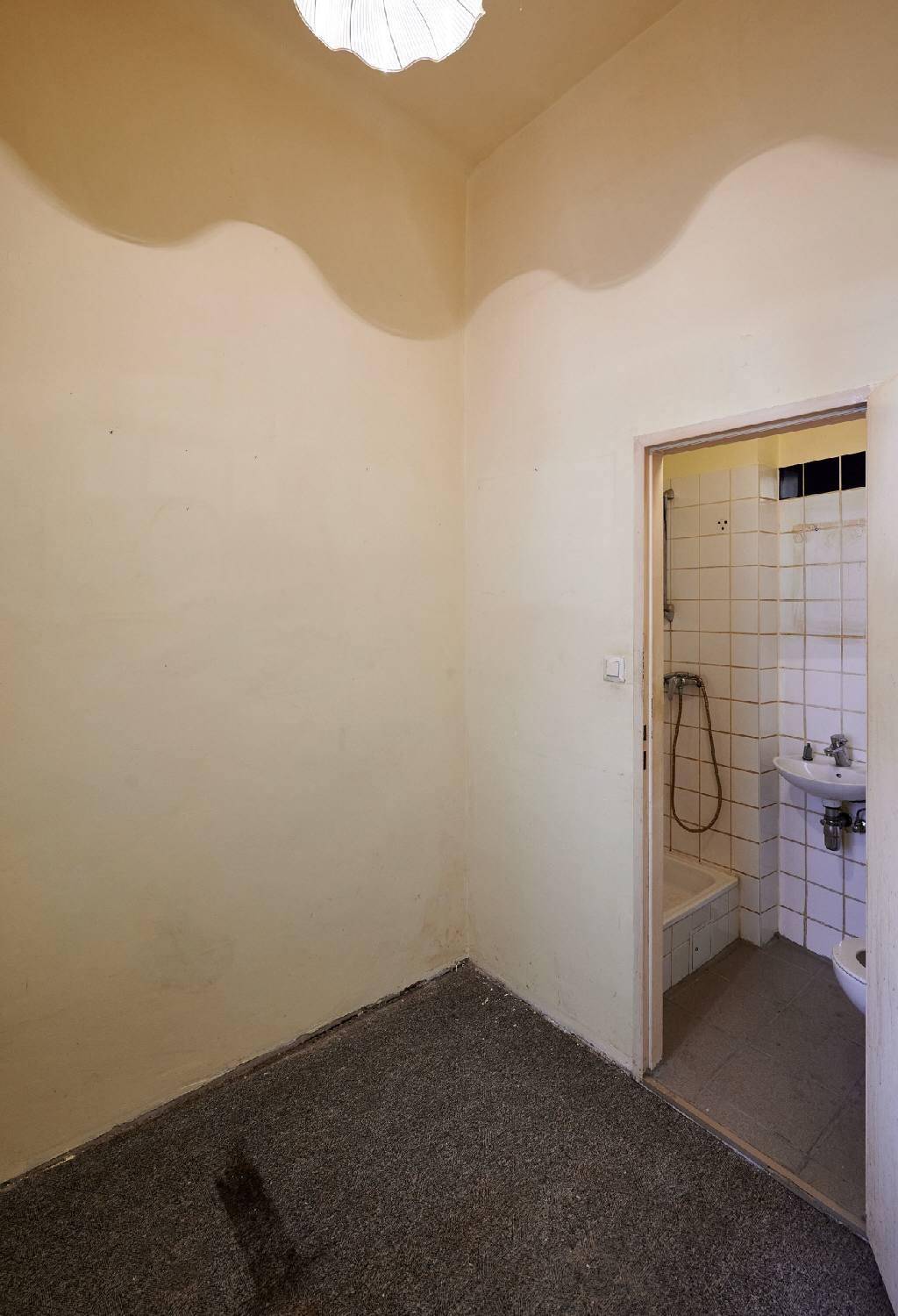 Kleiner Raum mit Terrazzoboden und Zugang zu einem Badezimmer mit Dusche und Waschbecken.