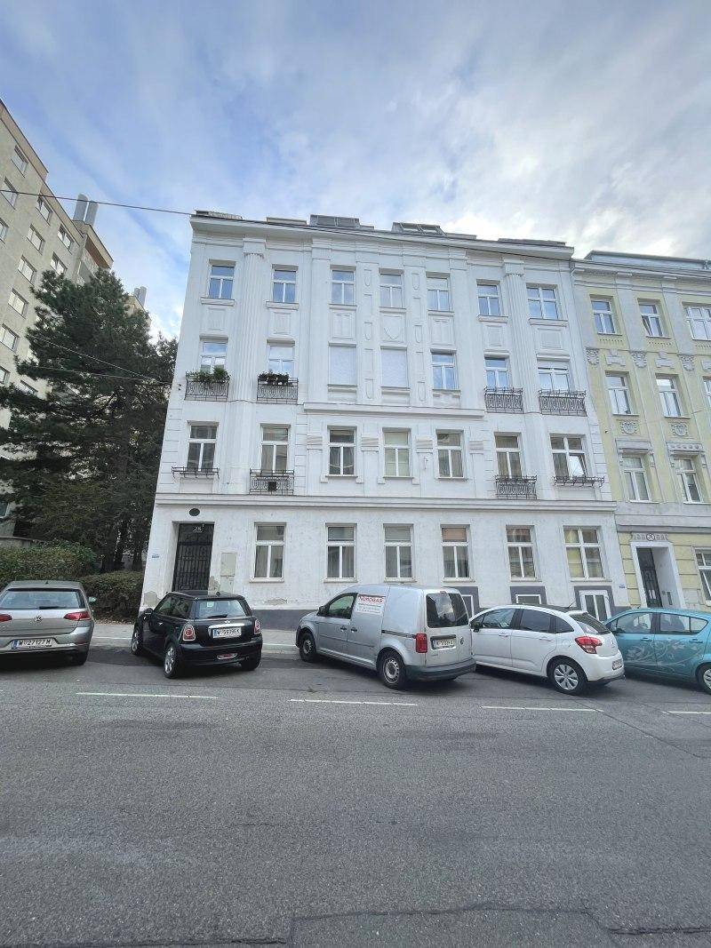 Klassisches Mehrfamilienhaus mit weißer Fassade und kleinen Balkonen an einer belebten Straße.