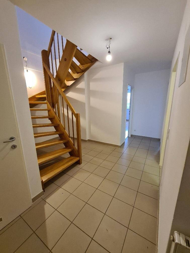 Heller Flur mit Fliesenboden und einer eleganten Holztreppe, die in die oberen Stockwerke führt.