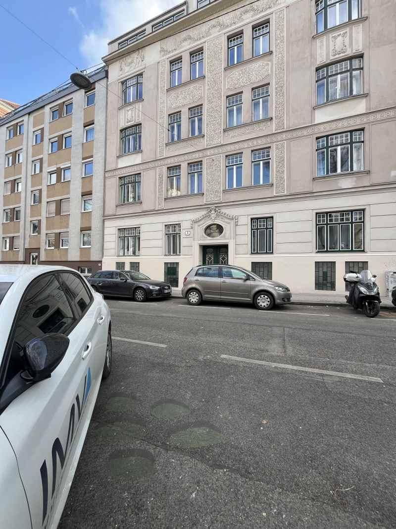Straßenansicht eines Altbaus mit dekorativer Fassade und parkenden Autos vor dem Gebäude.