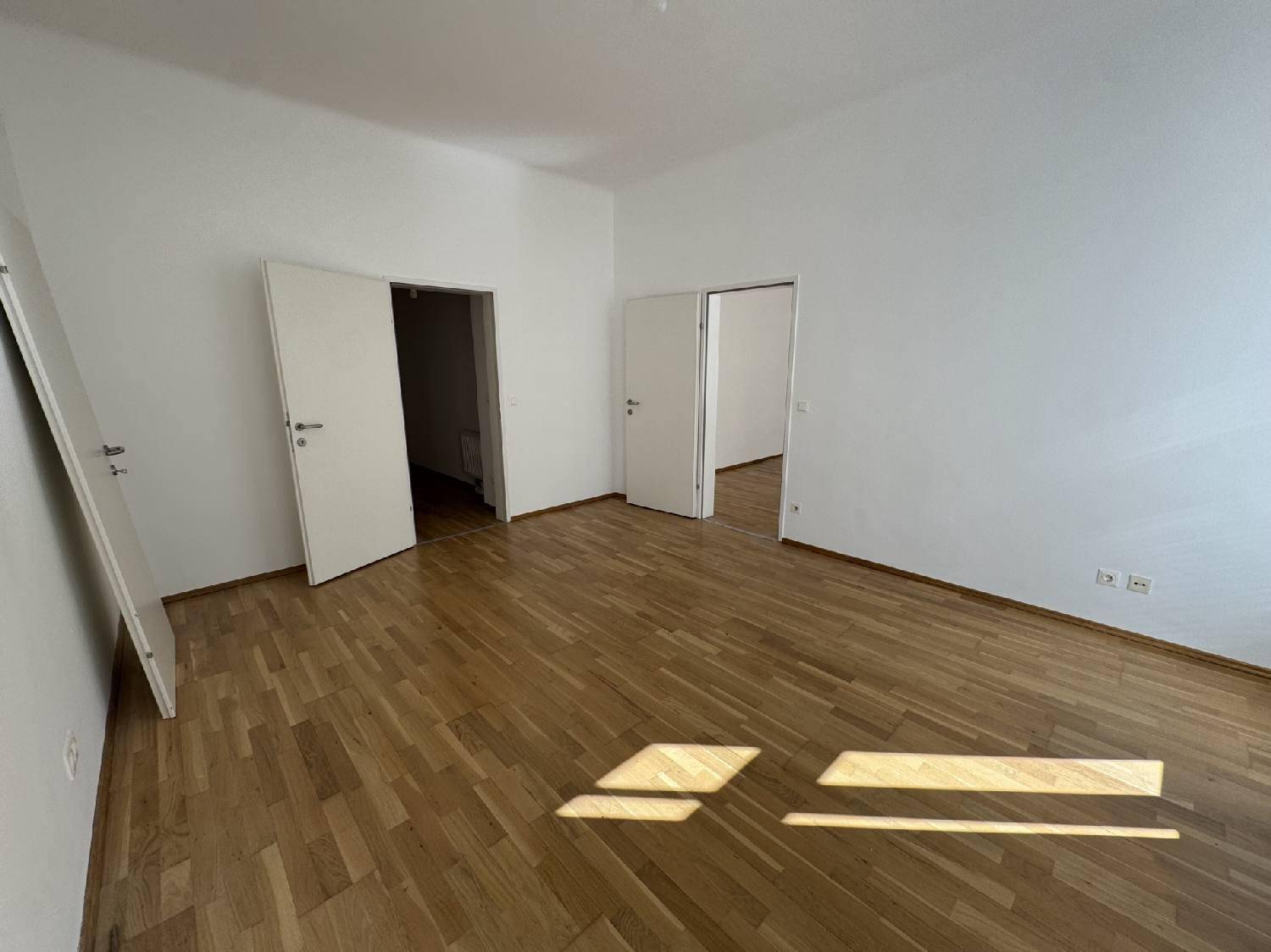 Helles Zimmer mit Parkettboden und mehreren Türen, die zu anderen Räumen führen, gut gepflegt.