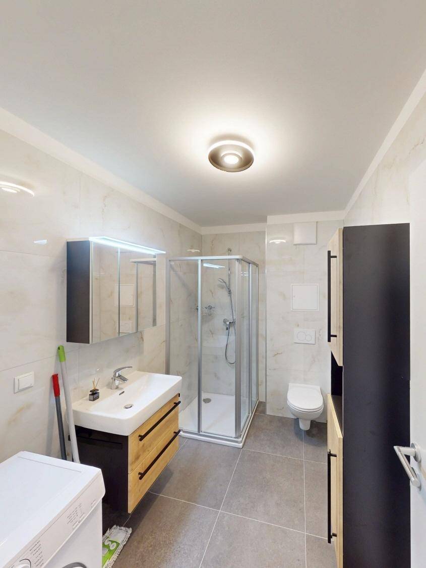 Modernes Badezimmer mit Duschkabine, Waschbecken, WC und Waschmaschine.