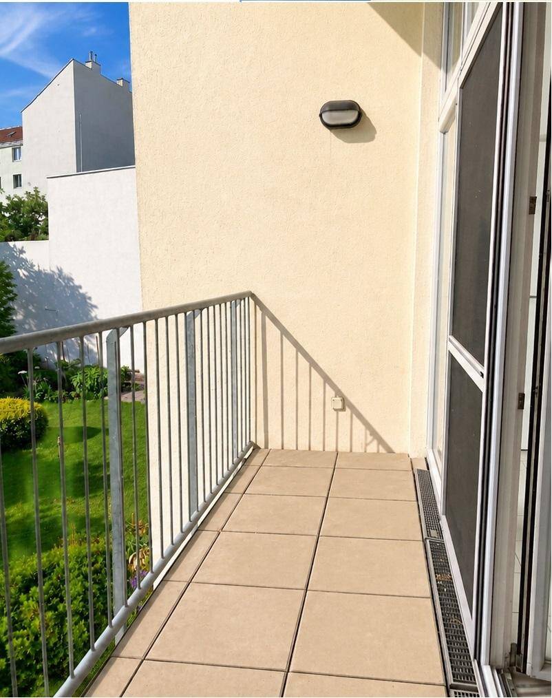 Heller Balkon mit Fliesenboden und Blick auf einen grünen Innenhof.