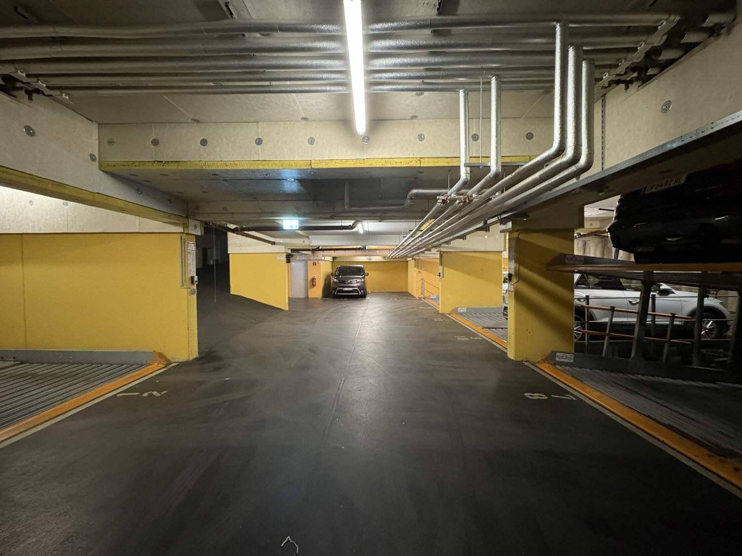 Langer Gang in einer Tiefgarage mit gelben Säulen und automatischen Parksystemen auf beiden Seiten.