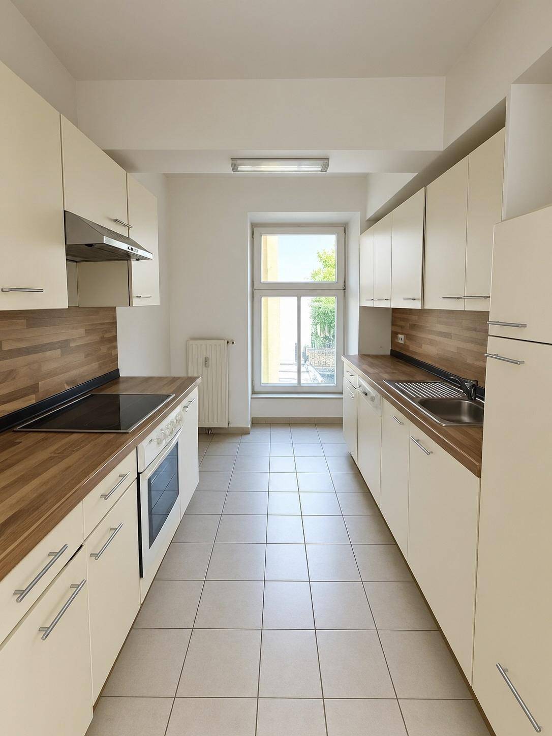 Funktionale Küche mit weißen Schränken, Holz-Arbeitsplatten und Fliesenboden, gut beleuchtet durch ein Fenster.
