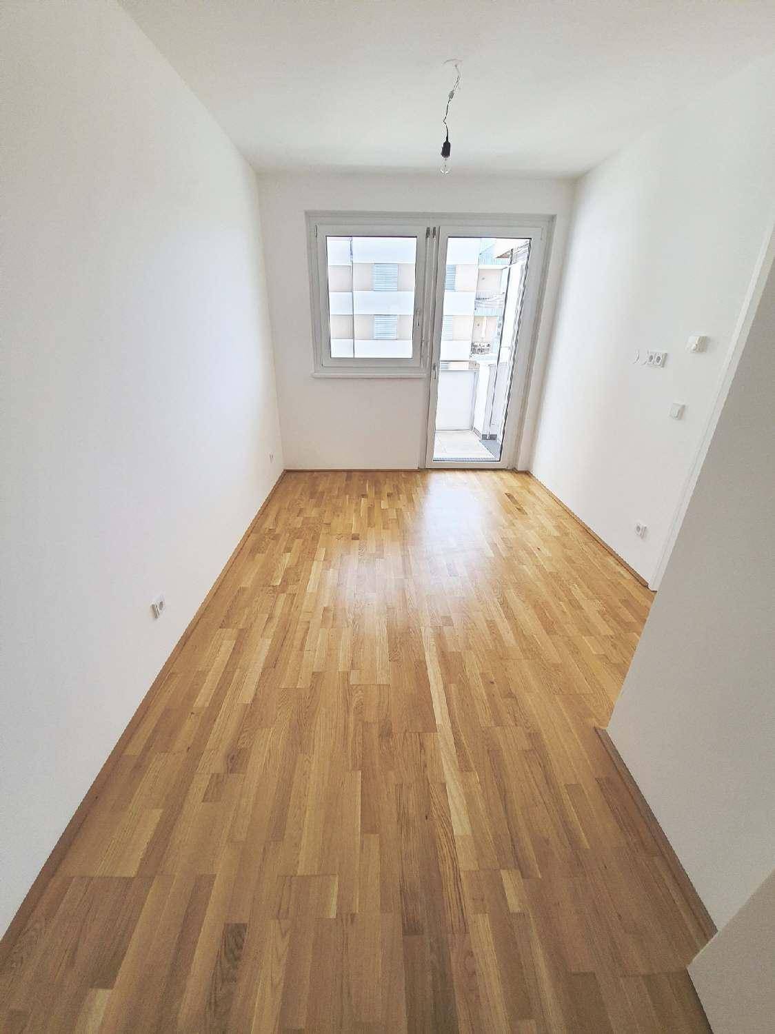 Heller Raum mit Parkettboden, weißen Wänden und Zugang zu einem Außenbereich.