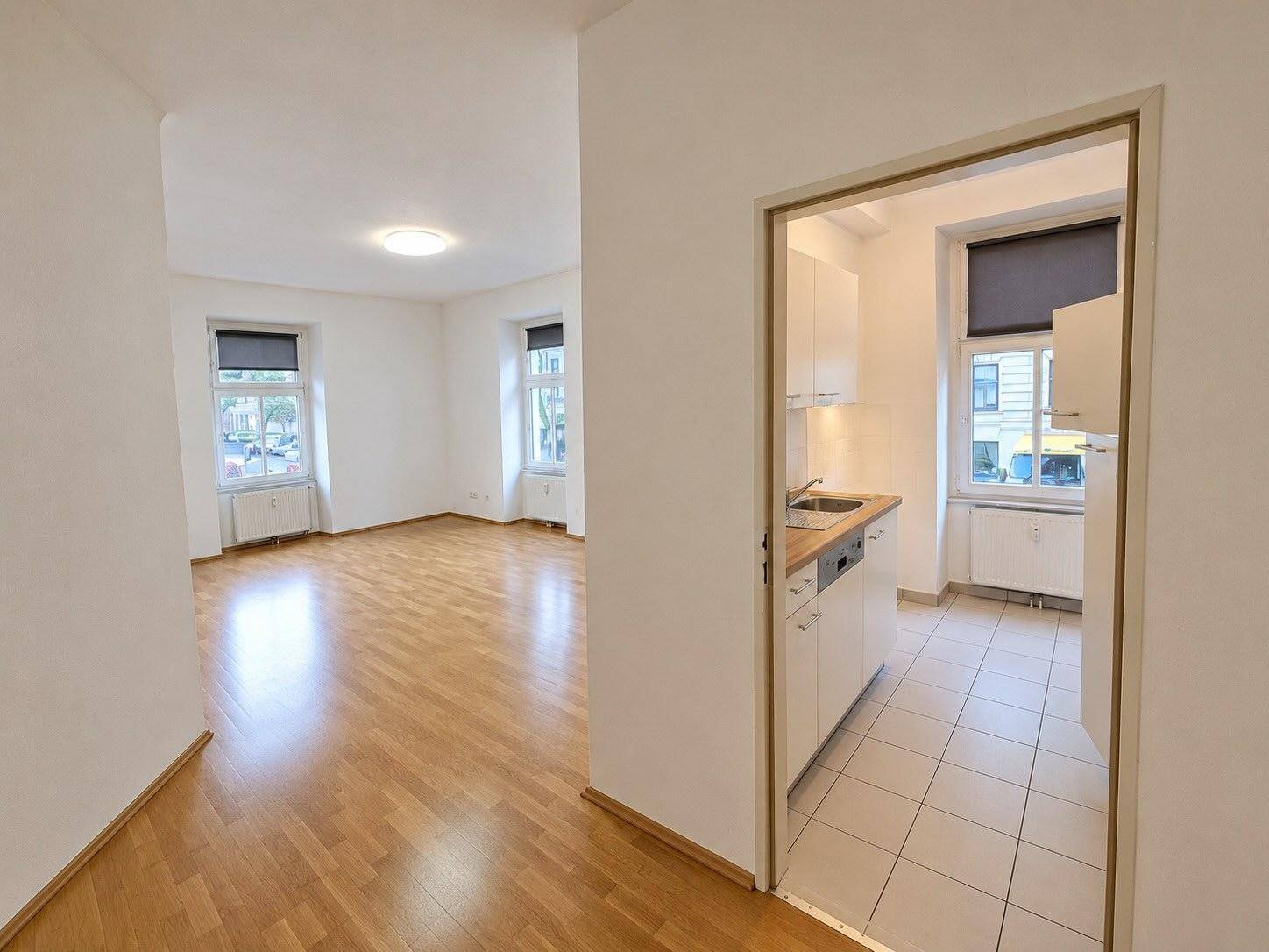 Heller Wohnbereich mit Parkettboden und Blick auf die separate, geflieste Küche durch eine Türöffnung.