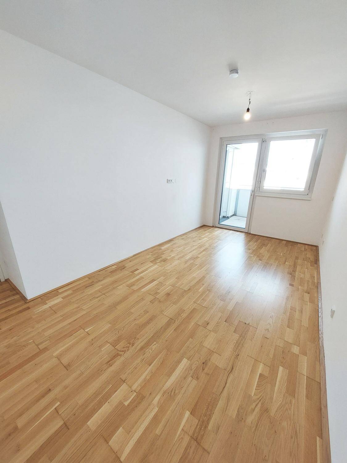 Schlafzimmer mit Parkettboden, großen Fenstern und Zugang zum Balkon.
