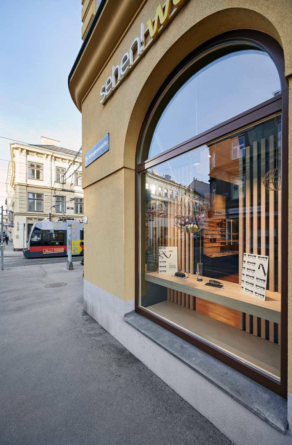 Detailansicht eines großen Rundbogen-Schaufensters an der Gebäudeecke mit Ausstellungsstücken im Inneren.
