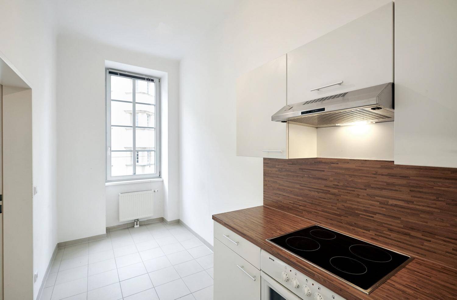 Helle Küche mit Fenster, weißen Schränken, Holzarbeitsplatte und Kochfeld.