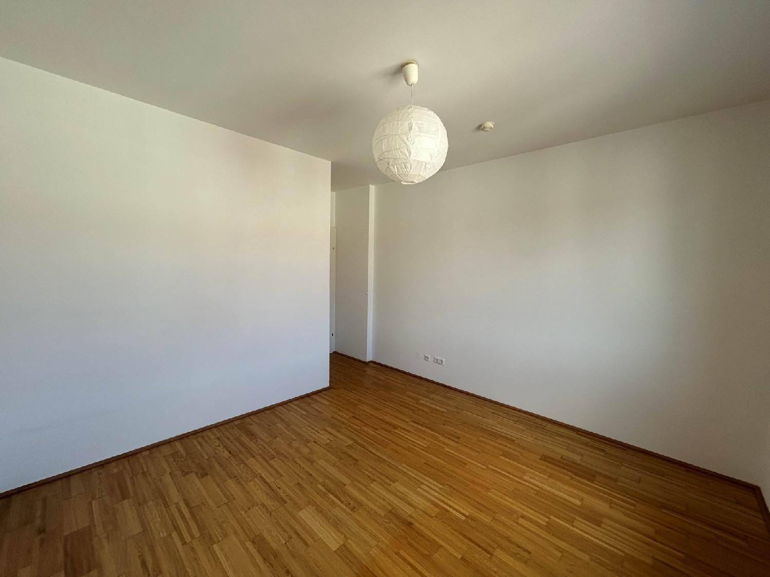 Unmöbliertes Zimmer mit Parkettboden und weiß gestrichenen Wänden, ideal für Schlaf- oder Arbeitsbereich.
