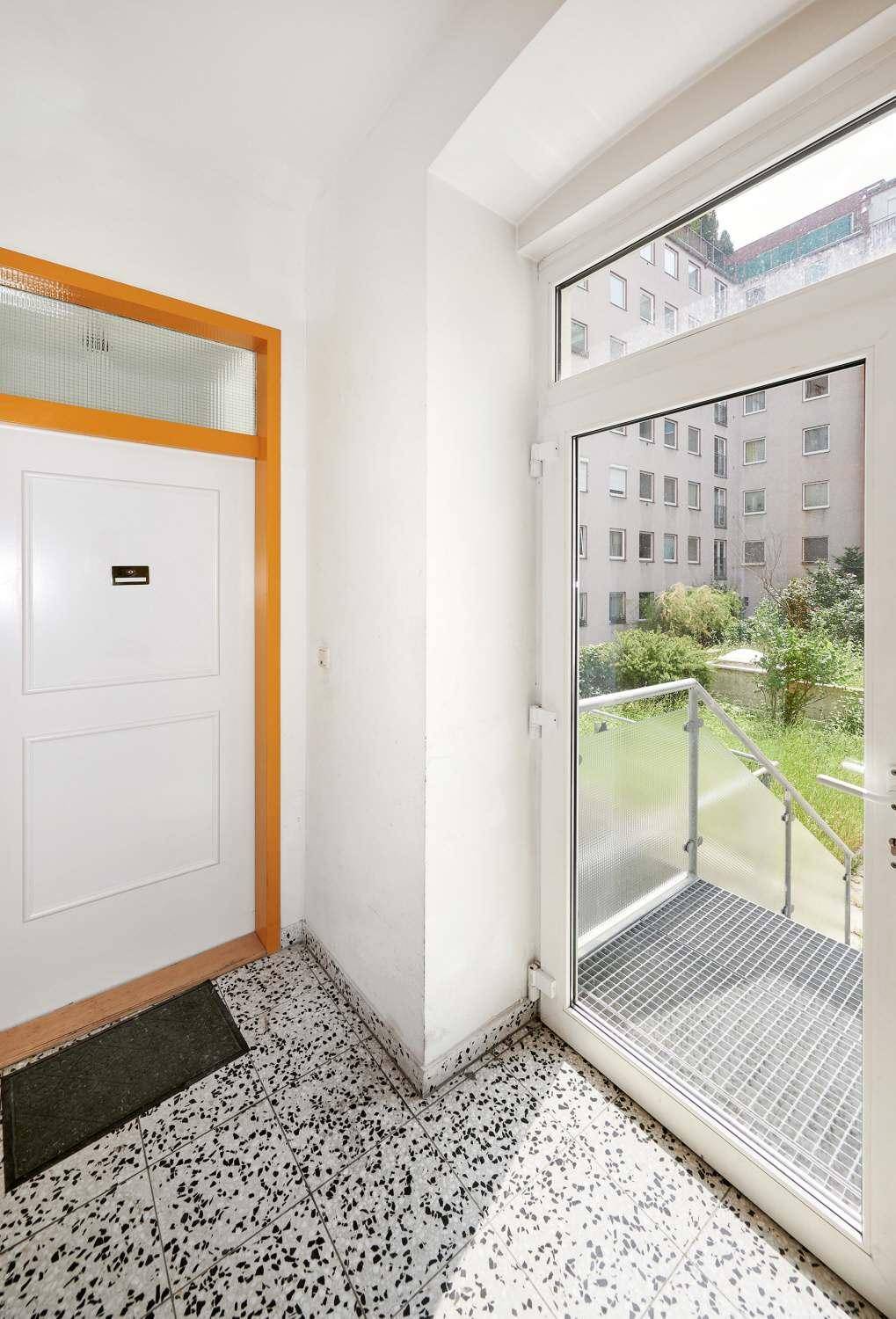 Eingangsbereich mit Terrazzoboden und großer Glastür, die zu einem Außenbereich führt.