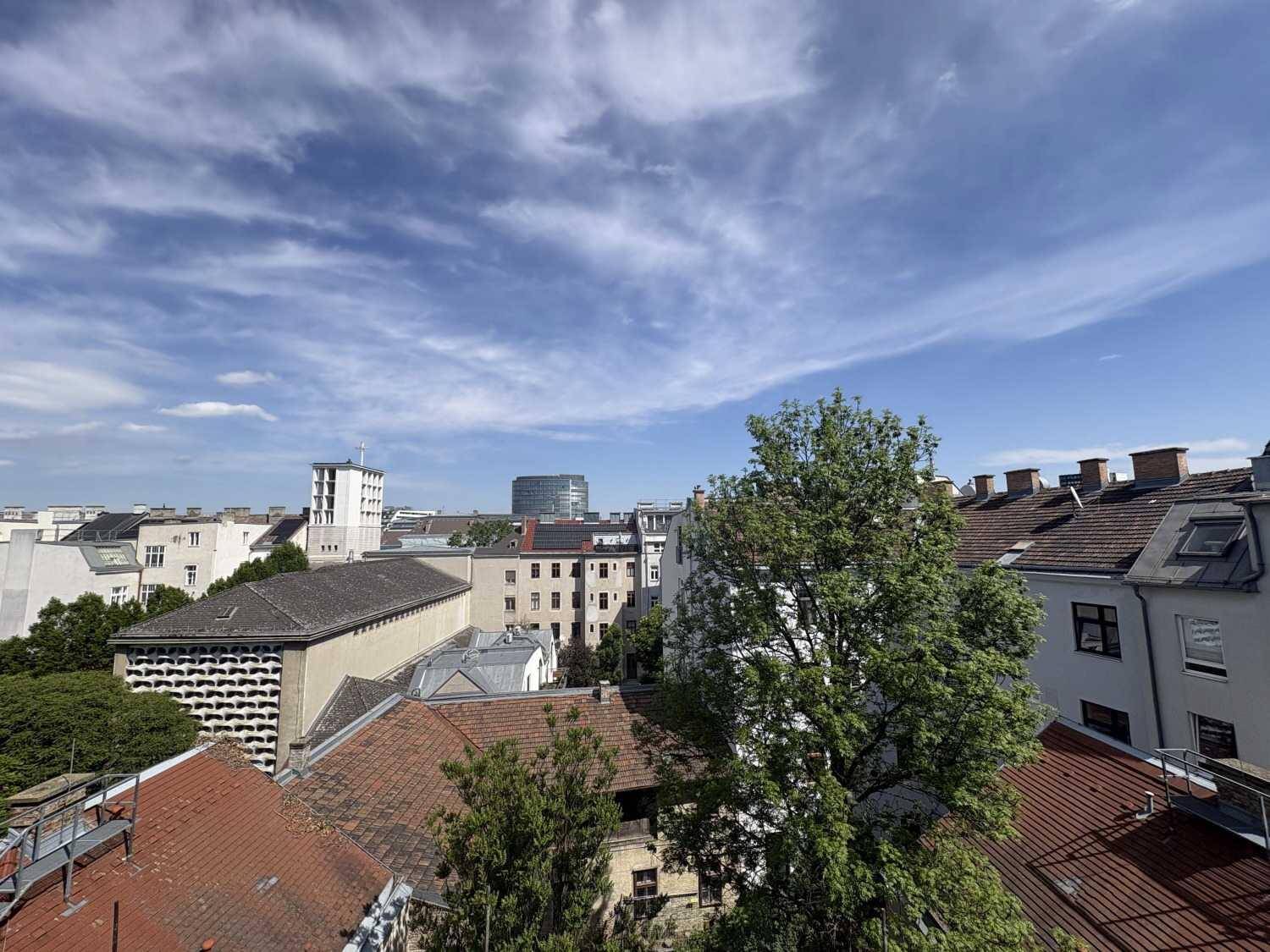 Panoramablick über die Dächer der Stadt mit Bäumen und blauem Himmel.