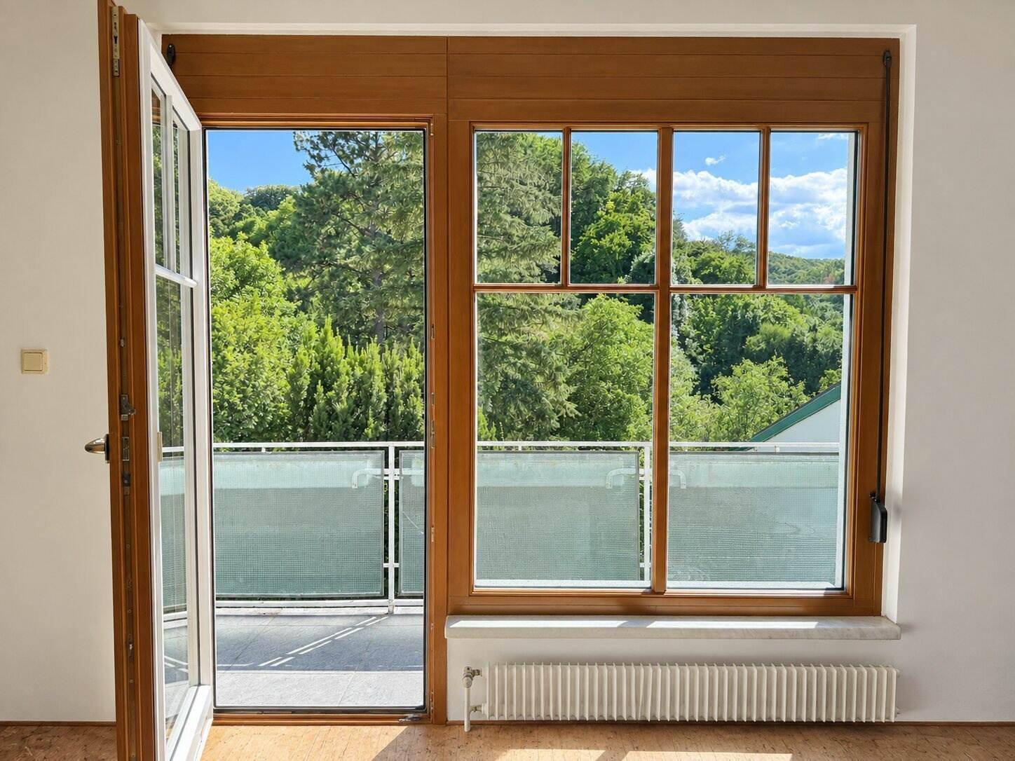 Heller Raum mit großem Fenster und Zugang zu einem Balkon mit weitem Grünblick.