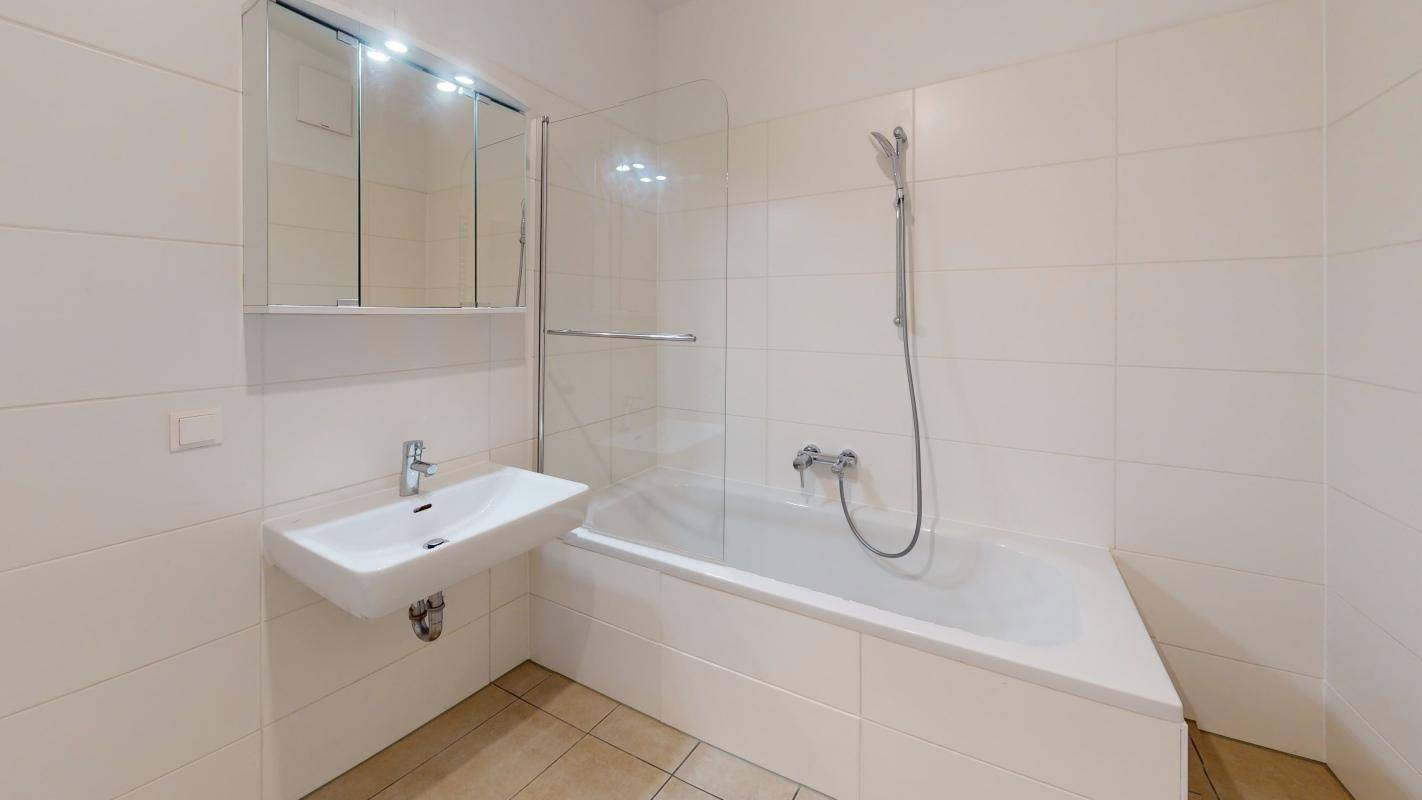 Funktionales Badezimmer mit Badewanne, integrierter Dusche und Wandspiegel.