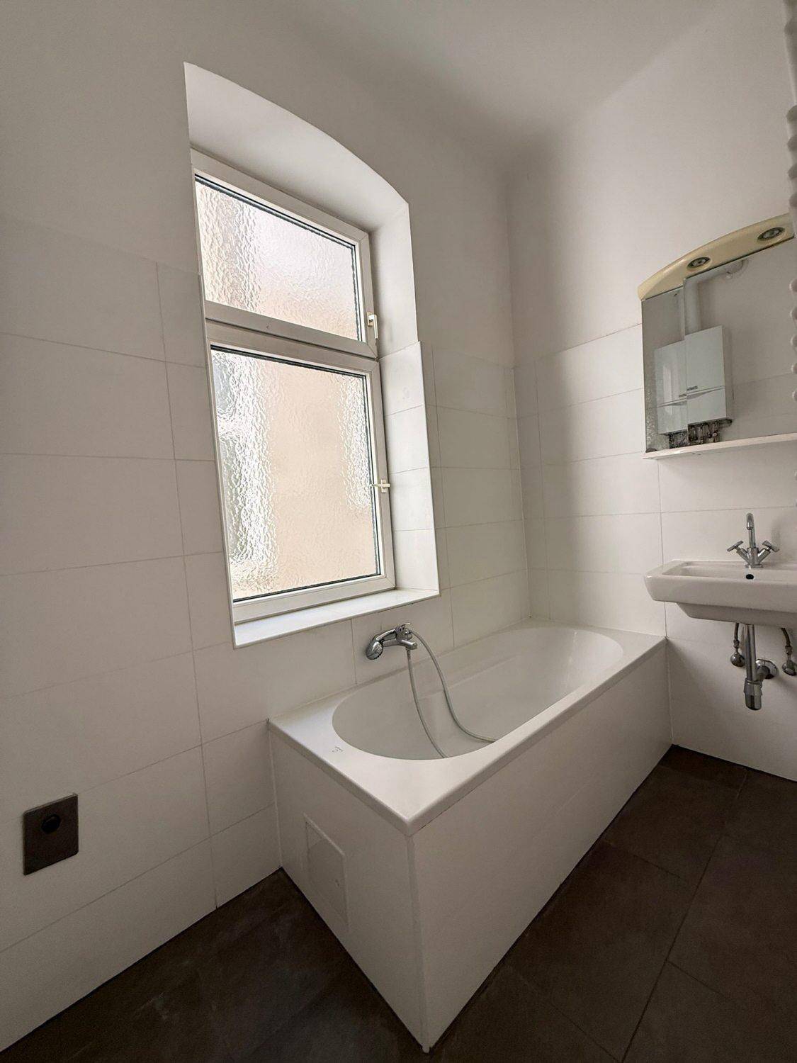 Gefliestes Badezimmer mit Badewanne, Waschbecken und einem Fenster für natürliche Belüftung.