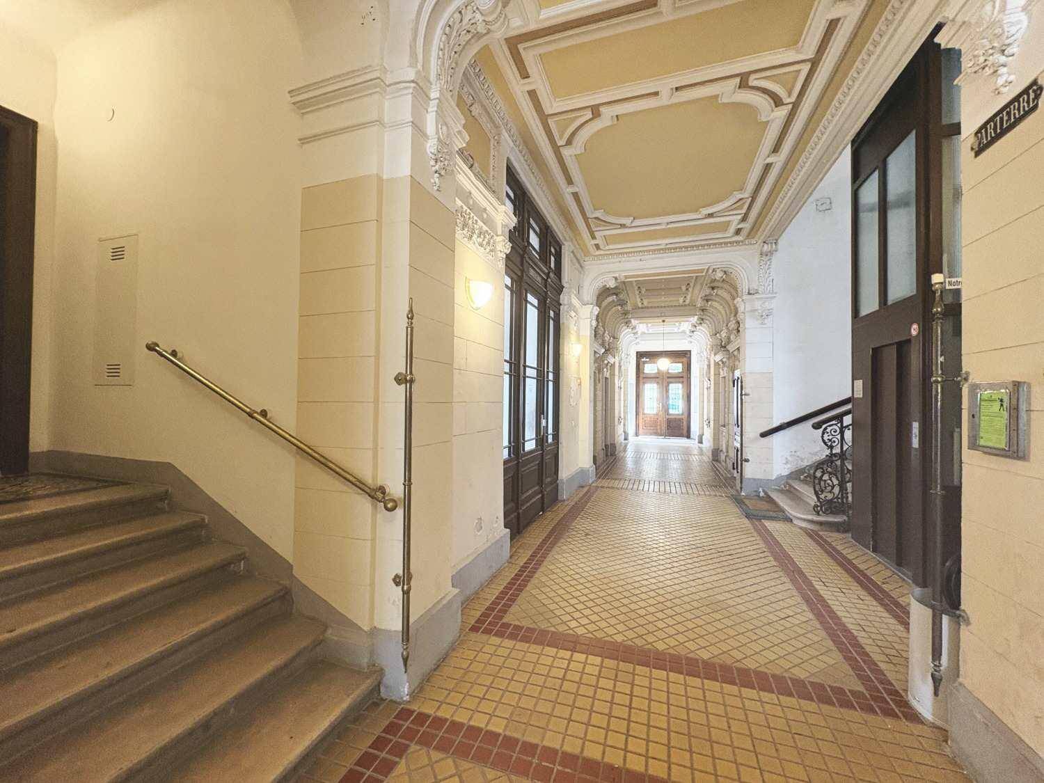 Langer, eleganter Flur mit verzierten Decken, Treppenaufgang und historischen Türen in einem Altbau.