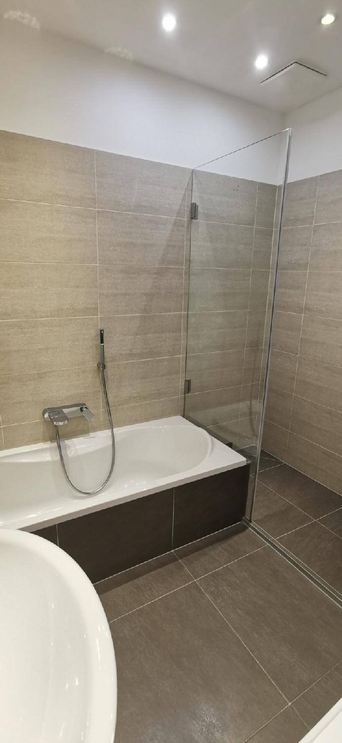 Zeitgemäßes Badezimmer mit Badewanne und separater Duschkabine, gefliest in warmen Beigetönen.
