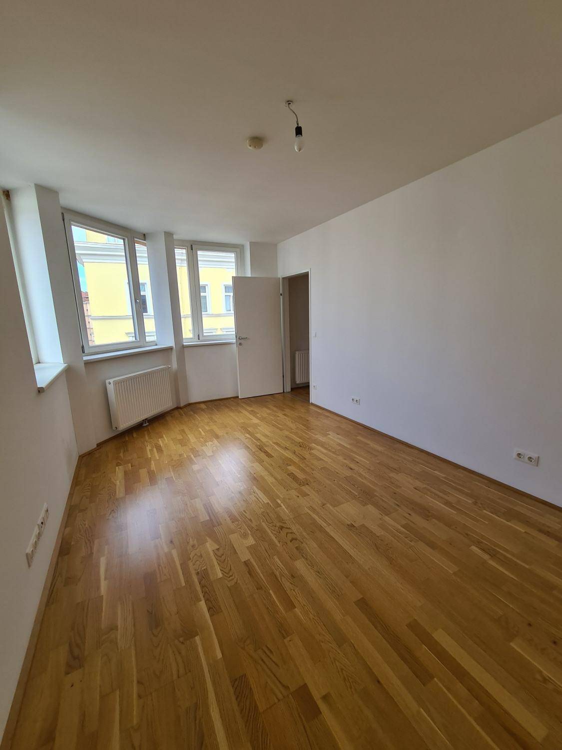 Helles Zimmer mit Parkettboden und großen Fenstern, die einen weiten Blick ermöglichen.