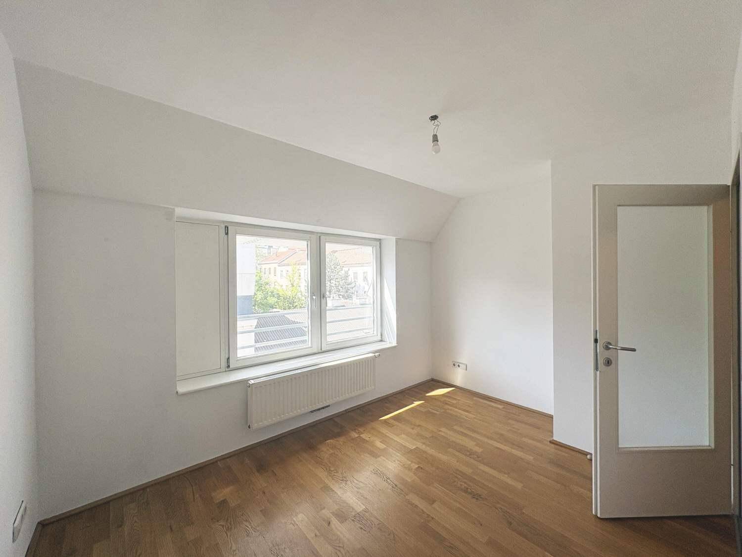 Freundliches Zimmer mit Holzboden und zwei Fenstern, bietet eine angenehme Atmosphäre.