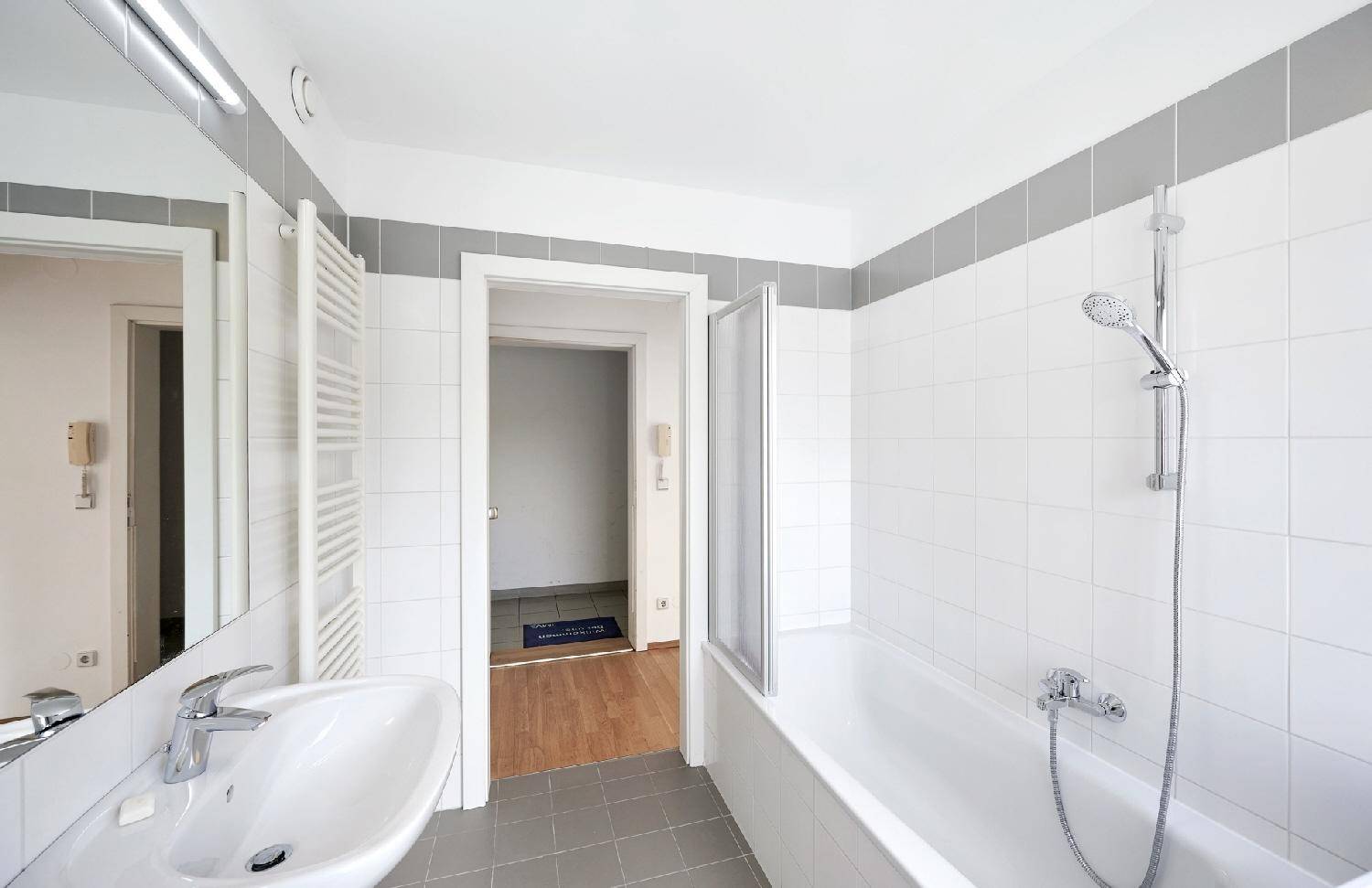 Badezimmer mit Badewanne, Duschfunktion, Waschbecken und großem Spiegel, angrenzend an einen Flur.