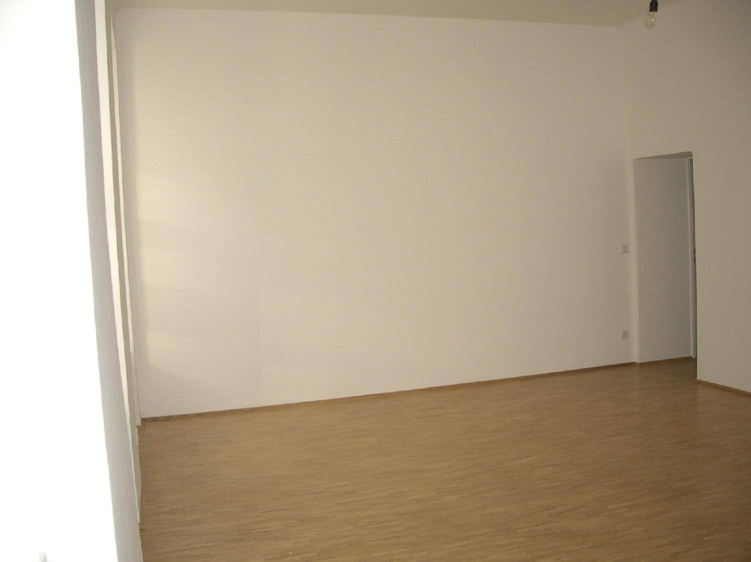 Leerer Raum mit hellem Holzboden und weißen Wänden, bereit für neue Einrichtungsideen.