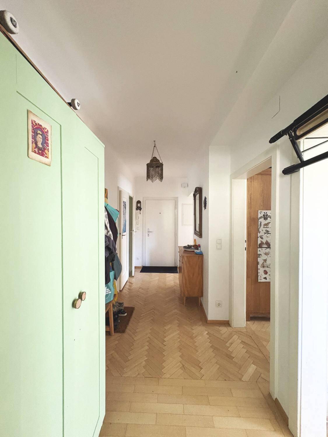 Heller Flur mit Fischgrätparkett, einem grünen Schrank und dekorativer Hängelampe.