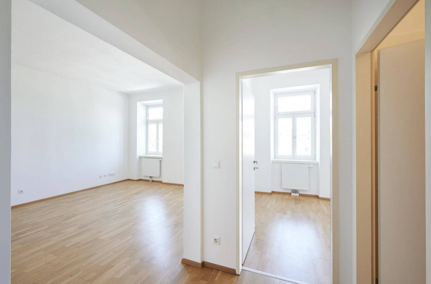 Offener Übergang zwischen zwei hellen Räumen mit Parkettboden und weißen Wänden.