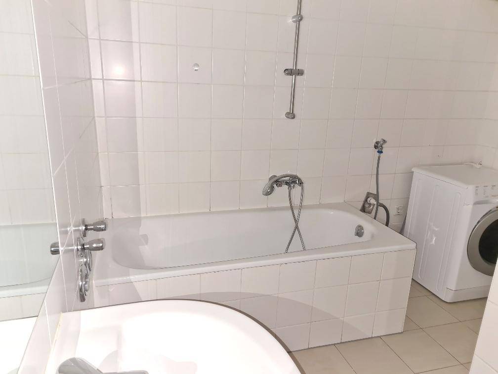 Helles Badezimmer mit Badewanne, Duschvorrichtung und Waschmaschine, komplett gefliest.