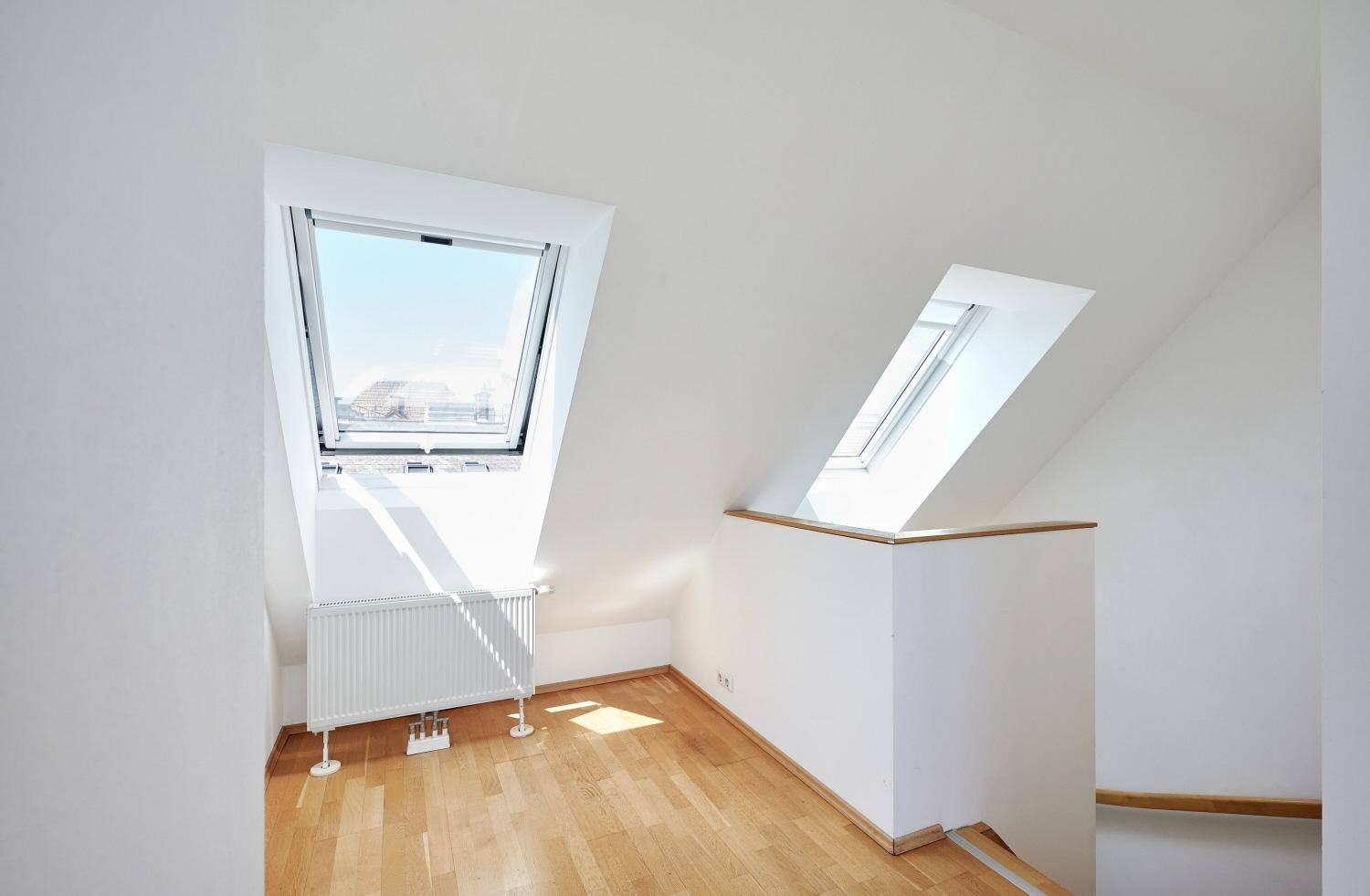 Heller Dachgeschossraum mit zwei großen Dachfenstern und Holzboden, ideal für ein Schlafzimmer.