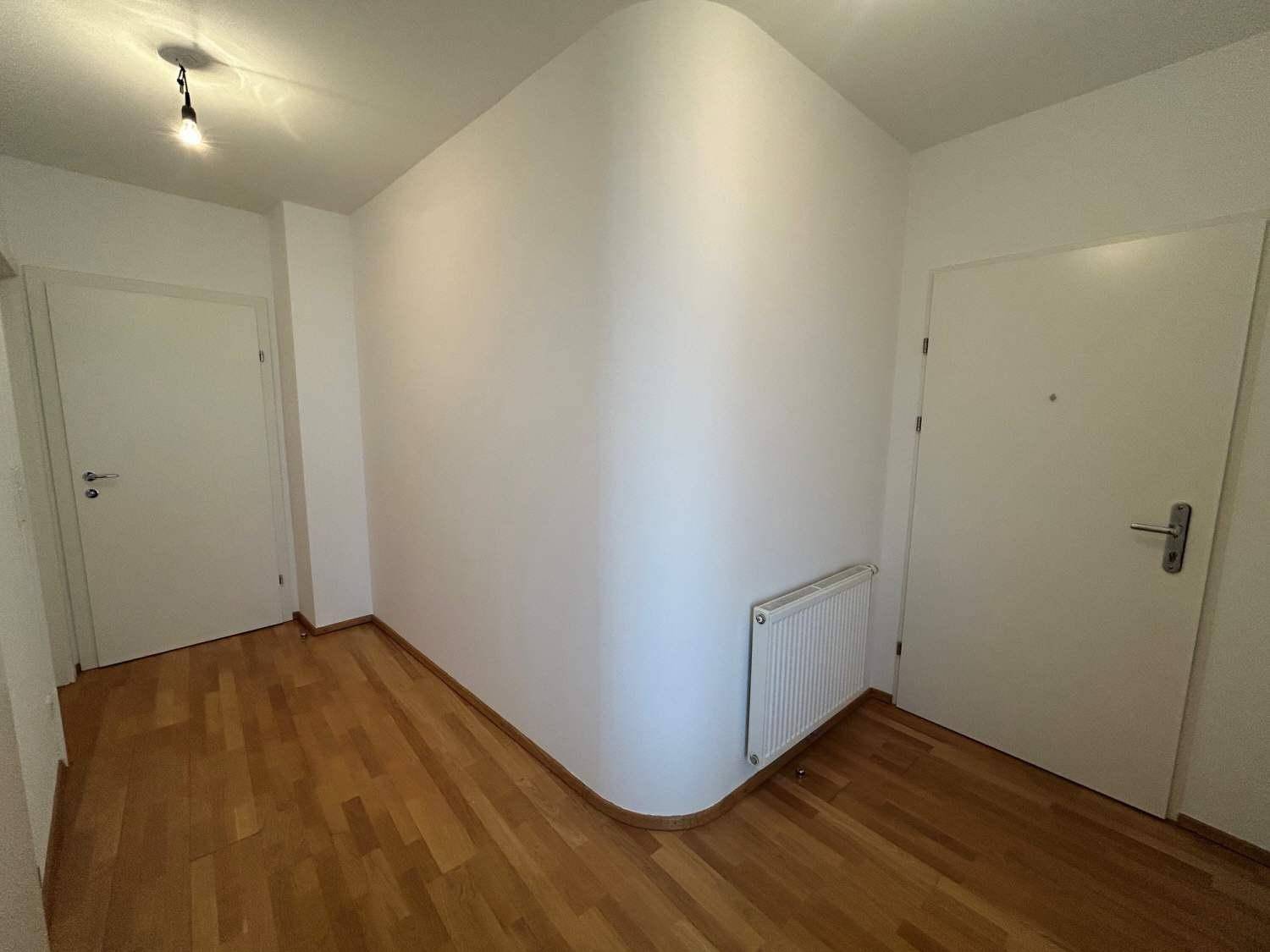 Heller Flur mit Parkettboden, weißen Wänden und Zugang zu weiteren Räumen.