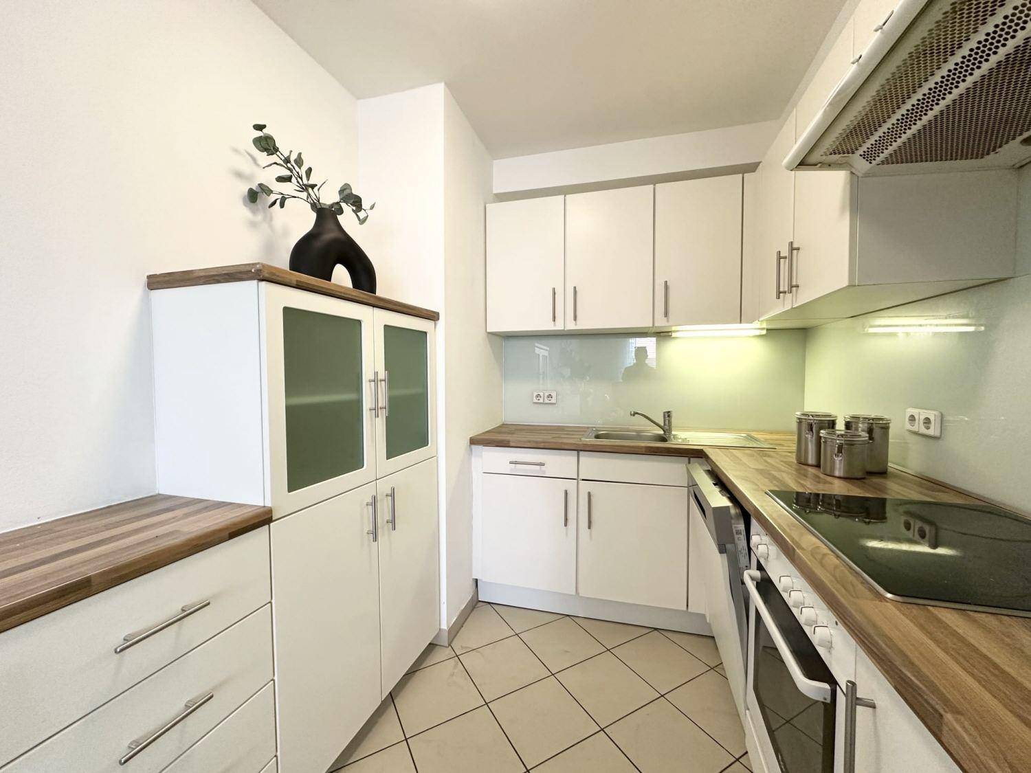 Funktionale Küche mit weißen Schränken, Holz-Arbeitsplatten und Fliesenboden.