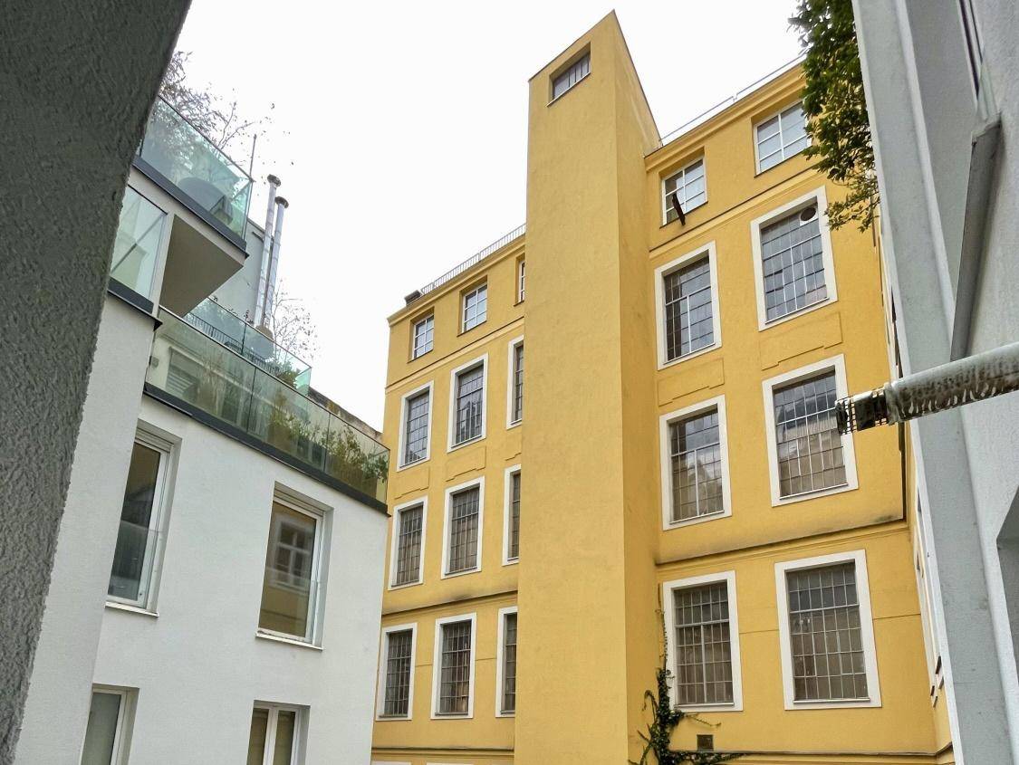 Blick in einen Innenhof mit einem modernen weißen Gebäude und einem älteren gelben Gebäude.