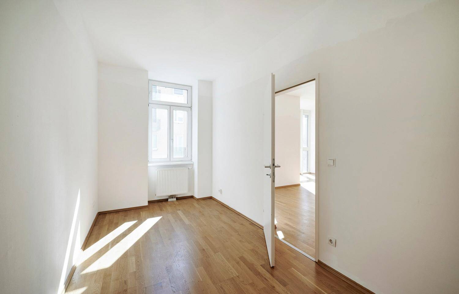 Heller Raum mit Parkettboden, weißen Wänden und einem Fenster, das viel Licht spendet.
