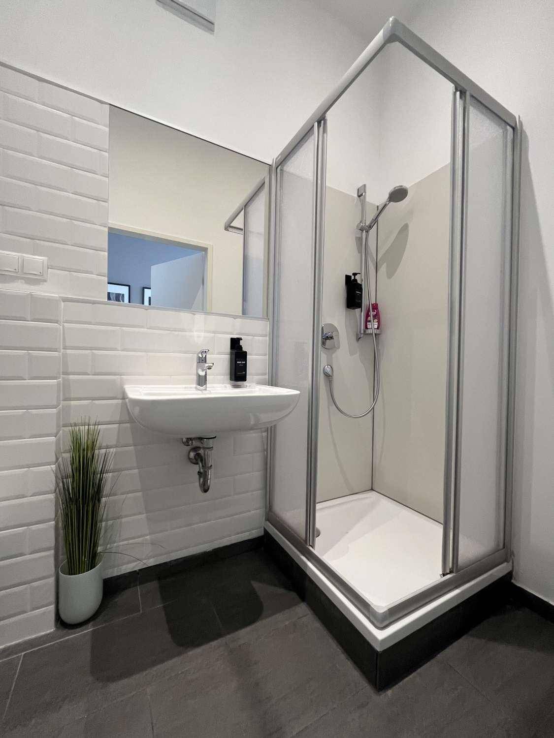 Modernes Badezimmer mit Duschkabine, weißen U-Bahn-Fliesen und dunklem Fliesenboden.