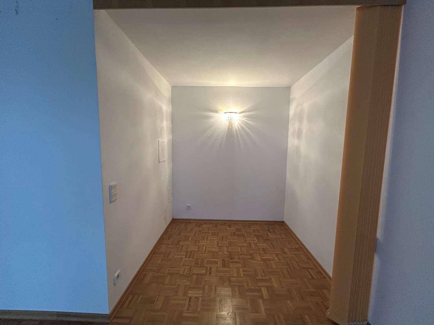 Kleiner, heller Nischenbereich mit Parkettboden und einer Wandleuchte, ideal als Arbeits- oder Abstellraum.