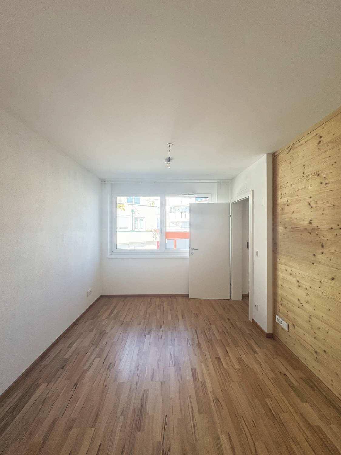 Freundliches Zimmer mit Holzboden, Fenster und einer Holzakzentwand für eine warme Atmosphäre.