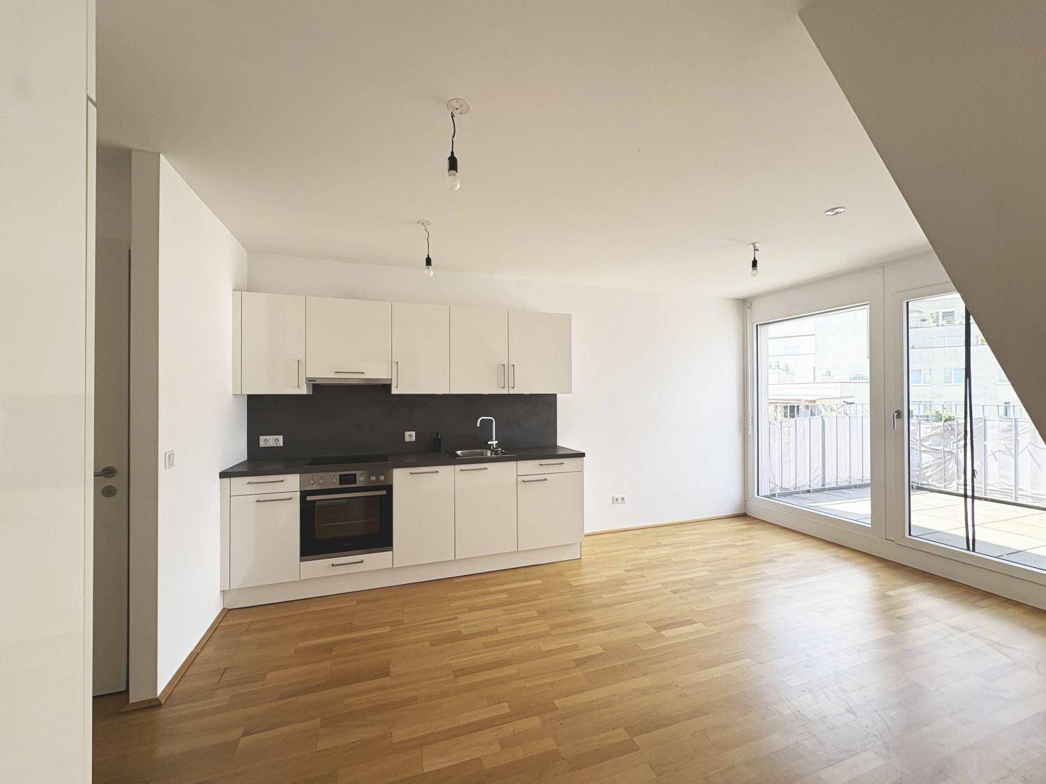 Moderne Einbauküche mit weißen Schränken und Holzboden, angrenzend an große Fenster.