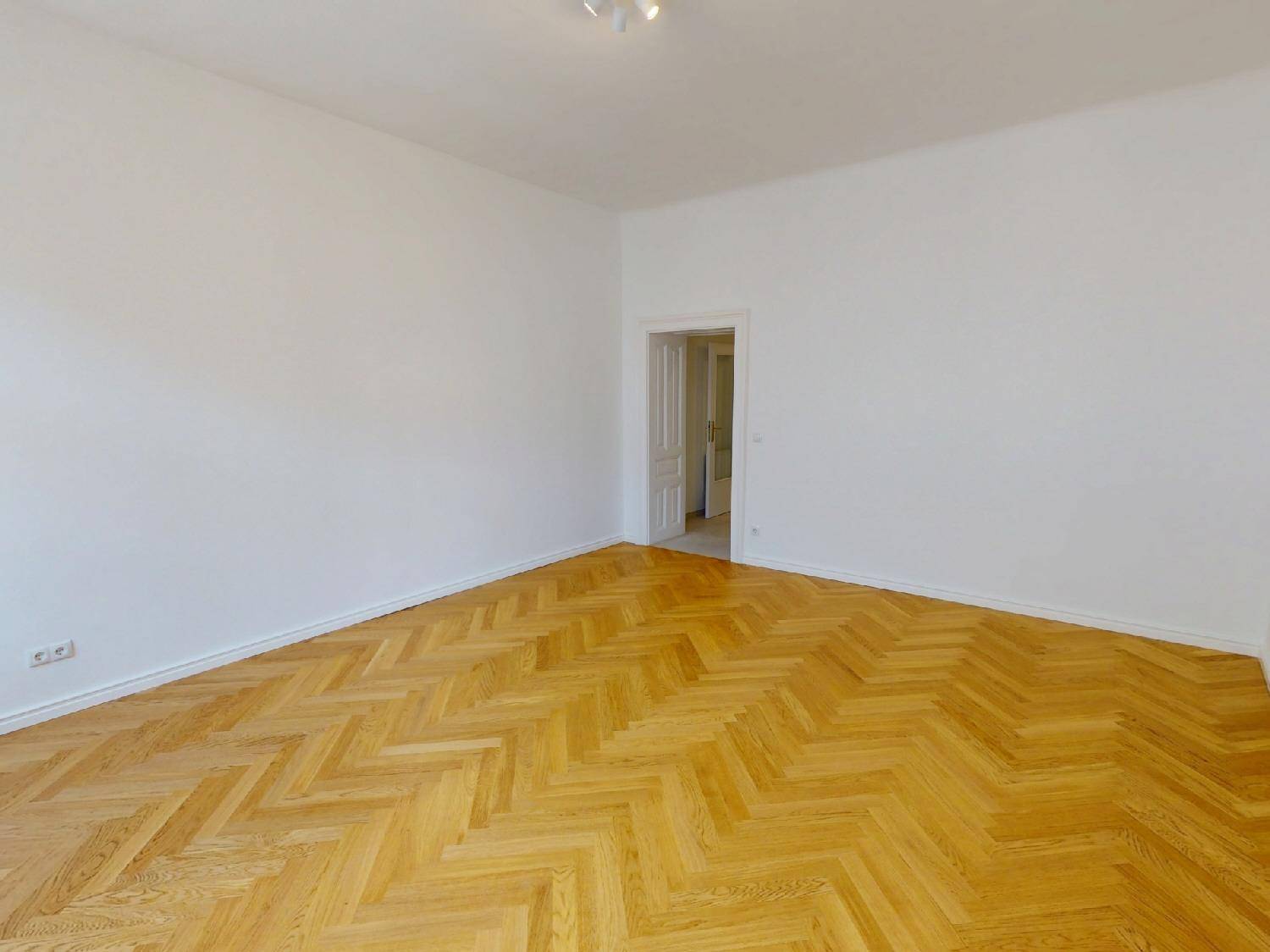 Geräumiges Zimmer mit klassischem Fischgrätparkett und weiß gestrichenen Wänden, bereit zur Einrichtung.