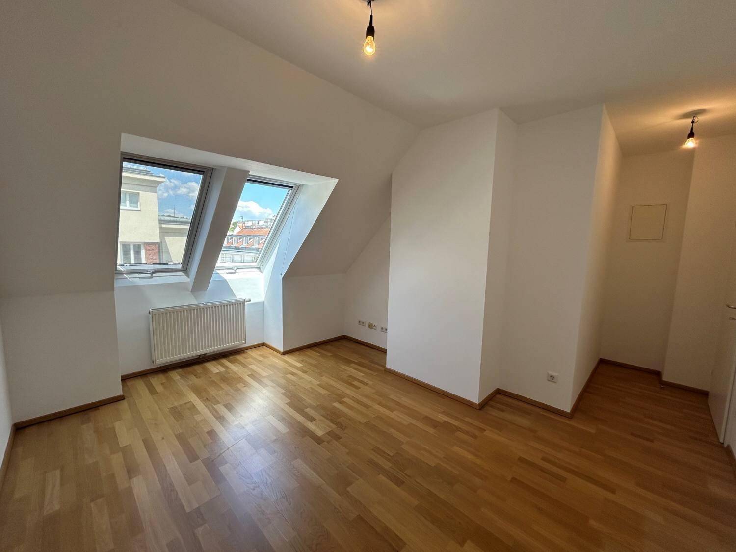 Helles Zimmer im Dachgeschoss mit Parkettboden, Dachschrägen und Dachfenstern.