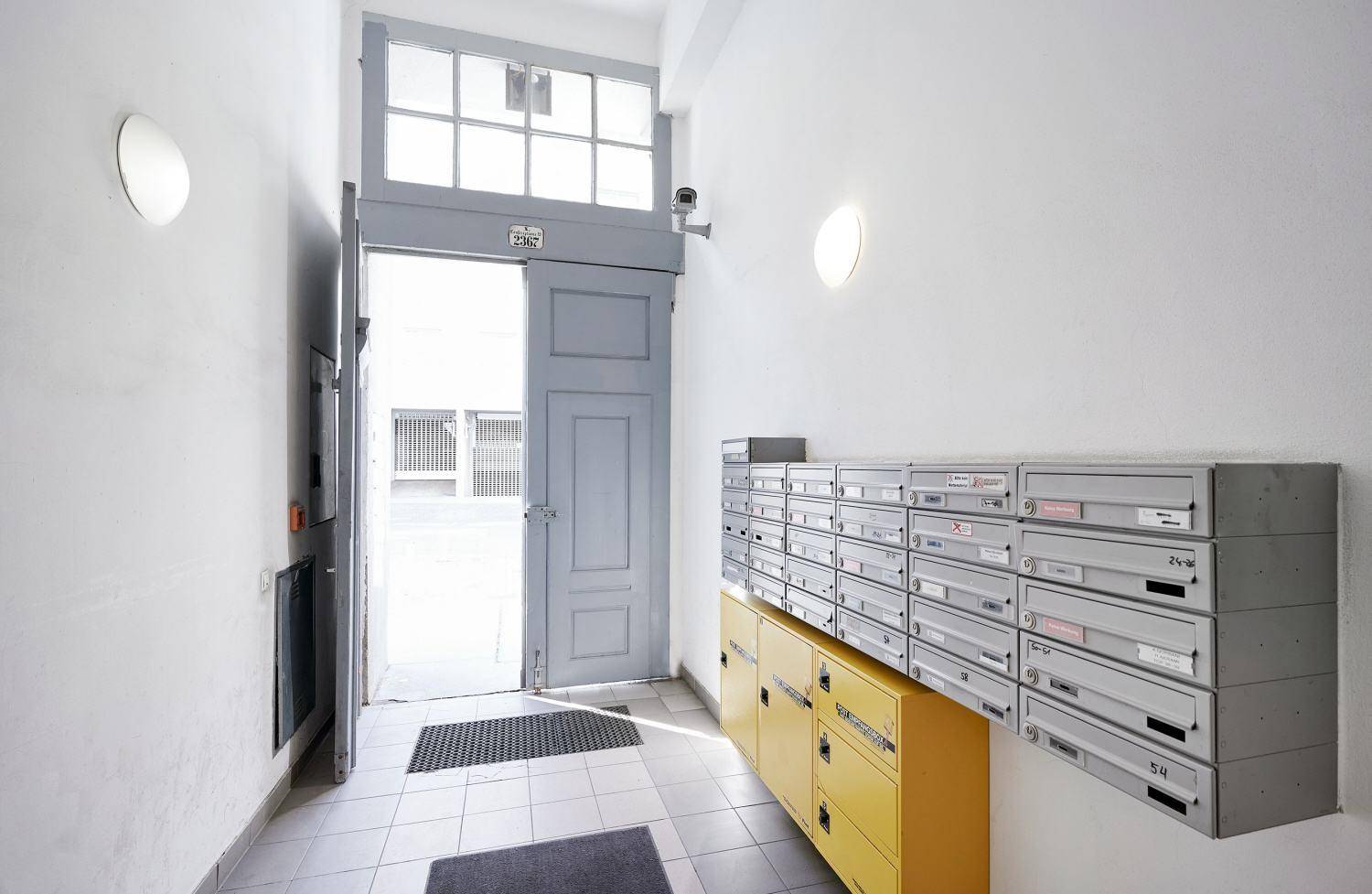 Heller Eingangsbereich mit Briefkästen und einer offenen Tür, die in einen Innenhof führt.