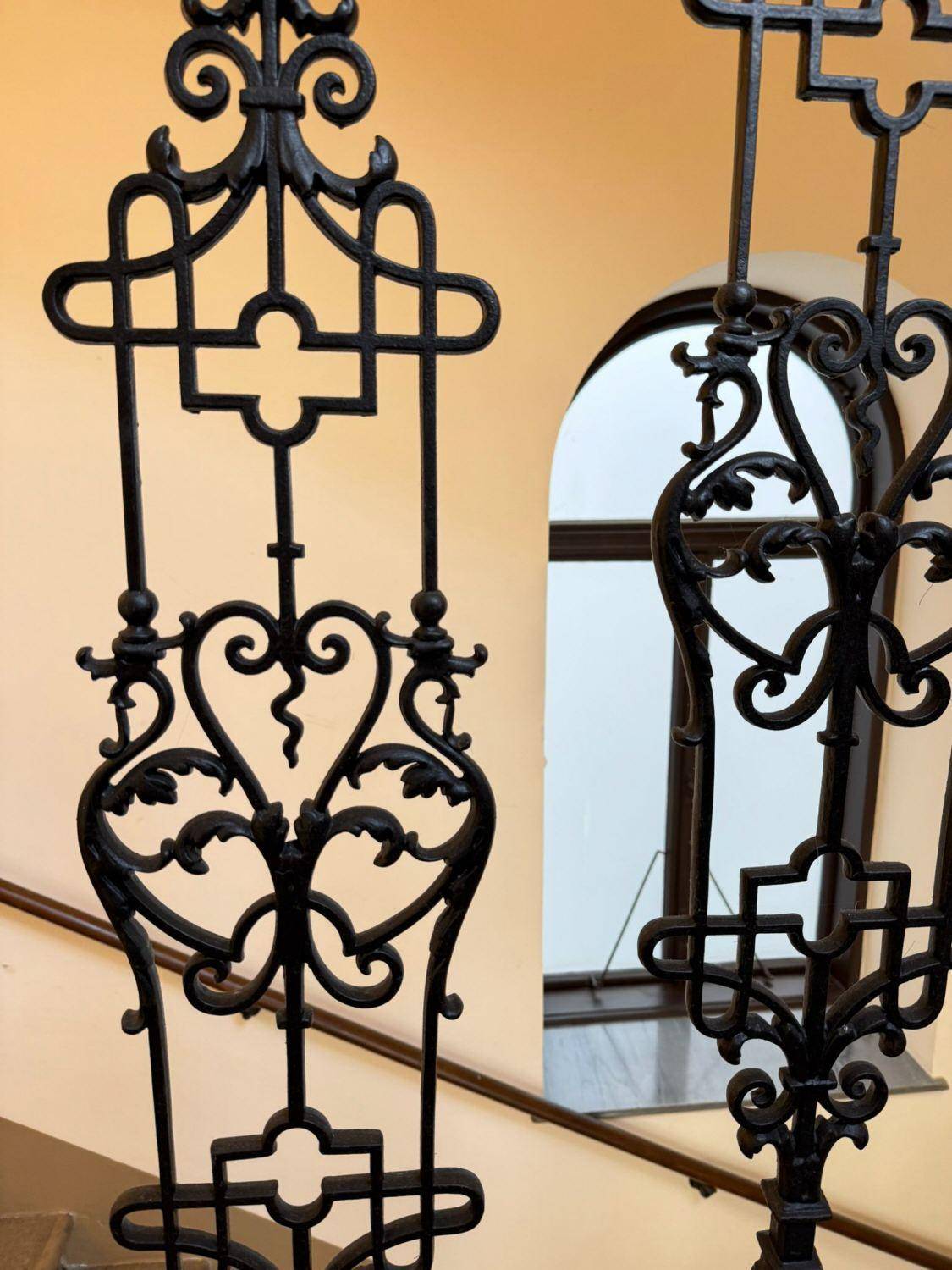 Detailaufnahme eines kunstvoll geschmiedeten, schwarzen Geländers im Treppenhaus eines Altbaus.