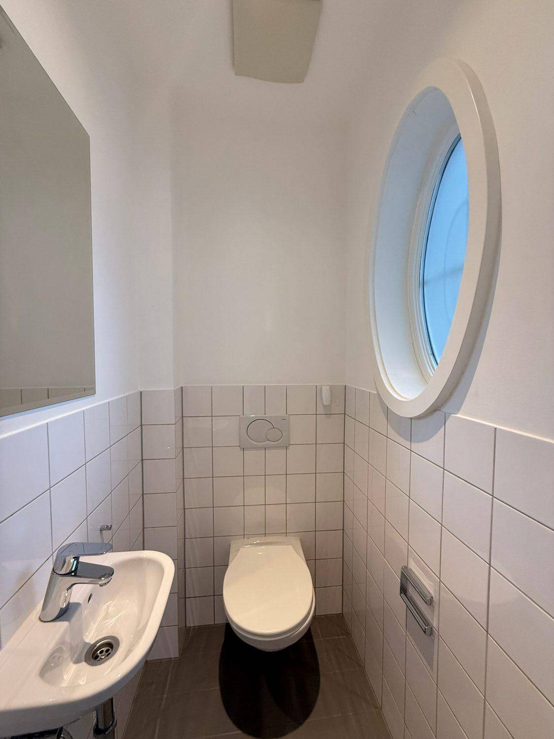 Kleines Gäste-WC mit Waschbecken, Toilette und einem einzigartigen runden Fenster.