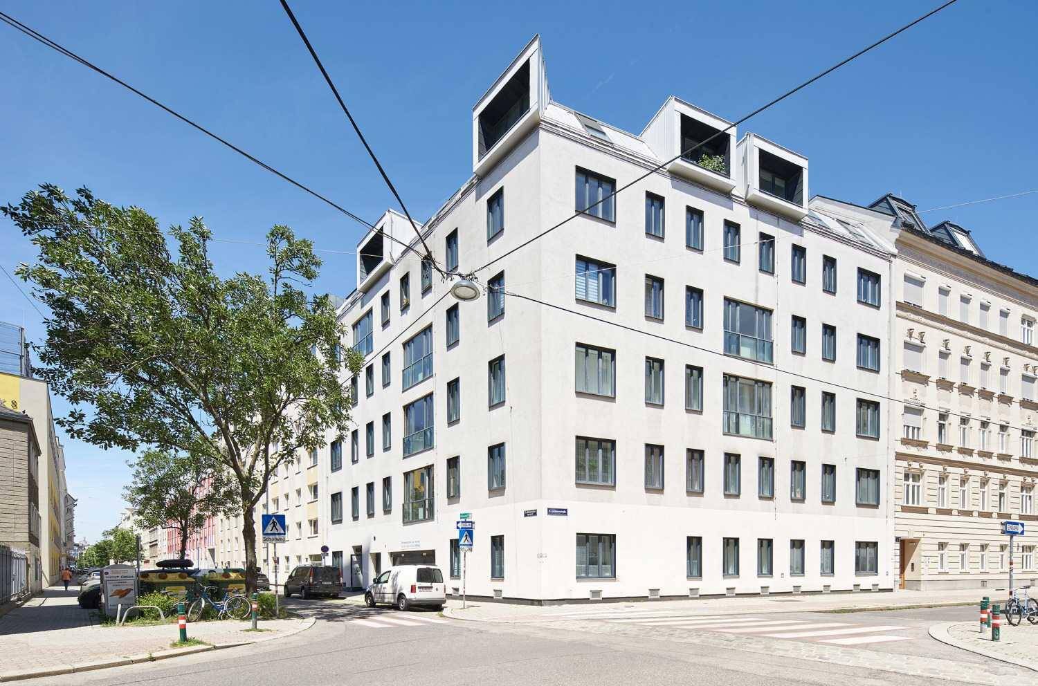 Modernes Eckgebäude mit vielen Fenstern an einer städtischen Kreuzung.