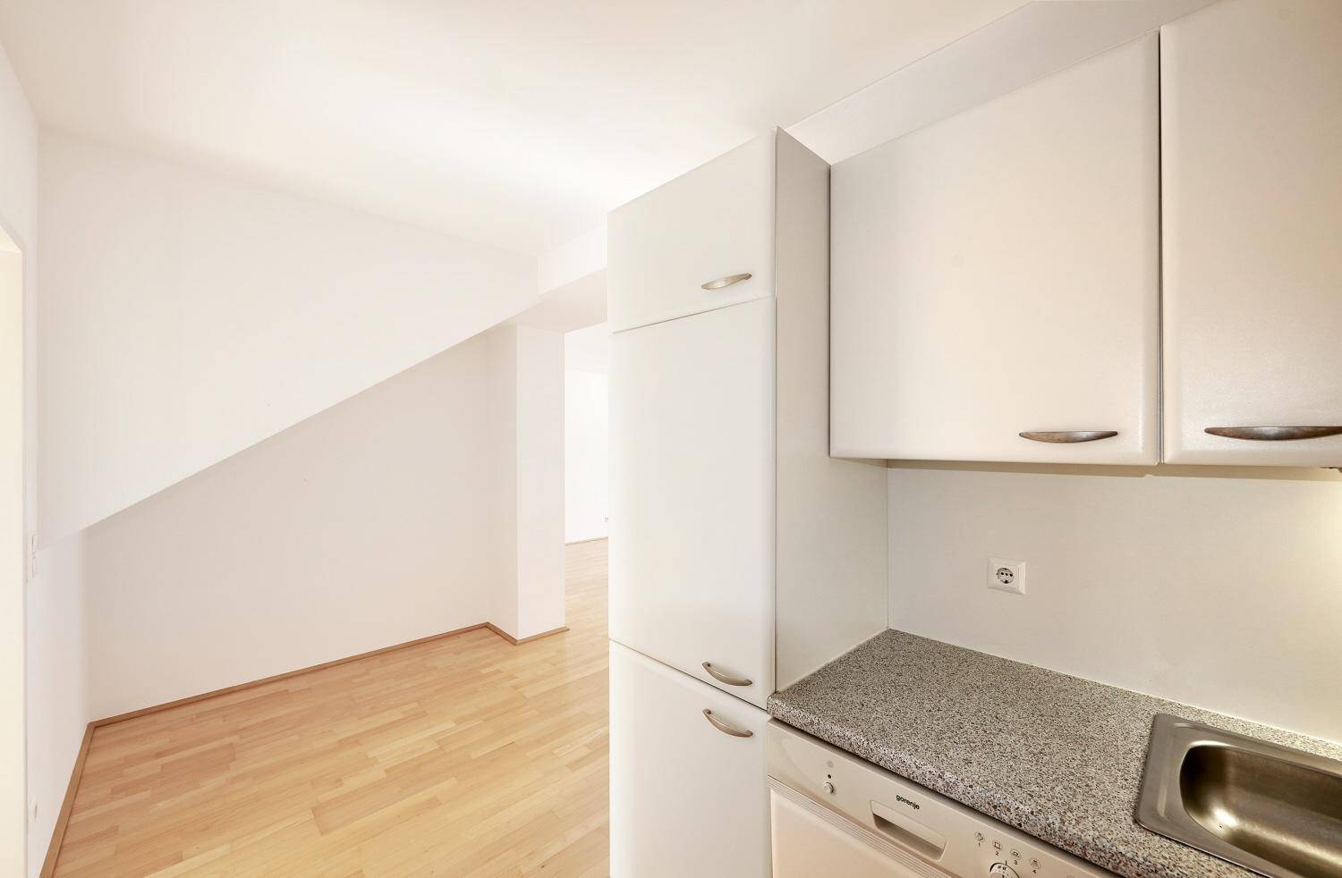 Detailansicht der weißen Küchenzeile mit Spüle, Arbeitsplatte und Blick in den hellen Raum mit Holzfußboden.
