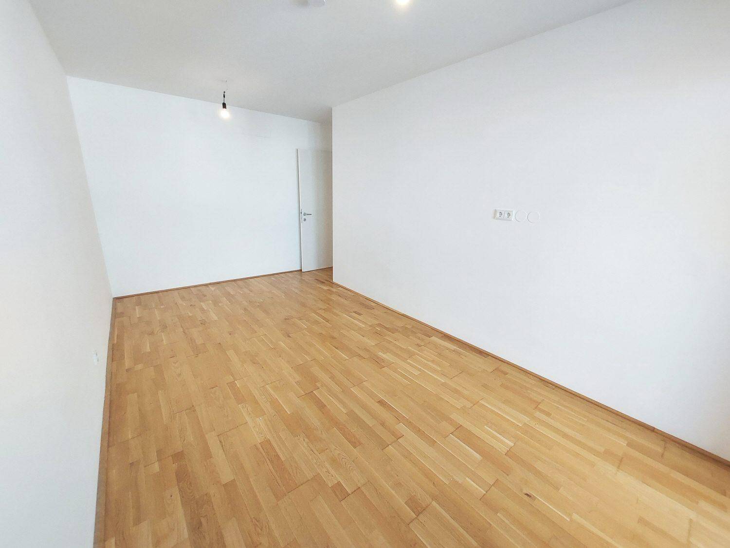 Leeres Schlafzimmer mit hellem Parkettboden und weißen Wänden.