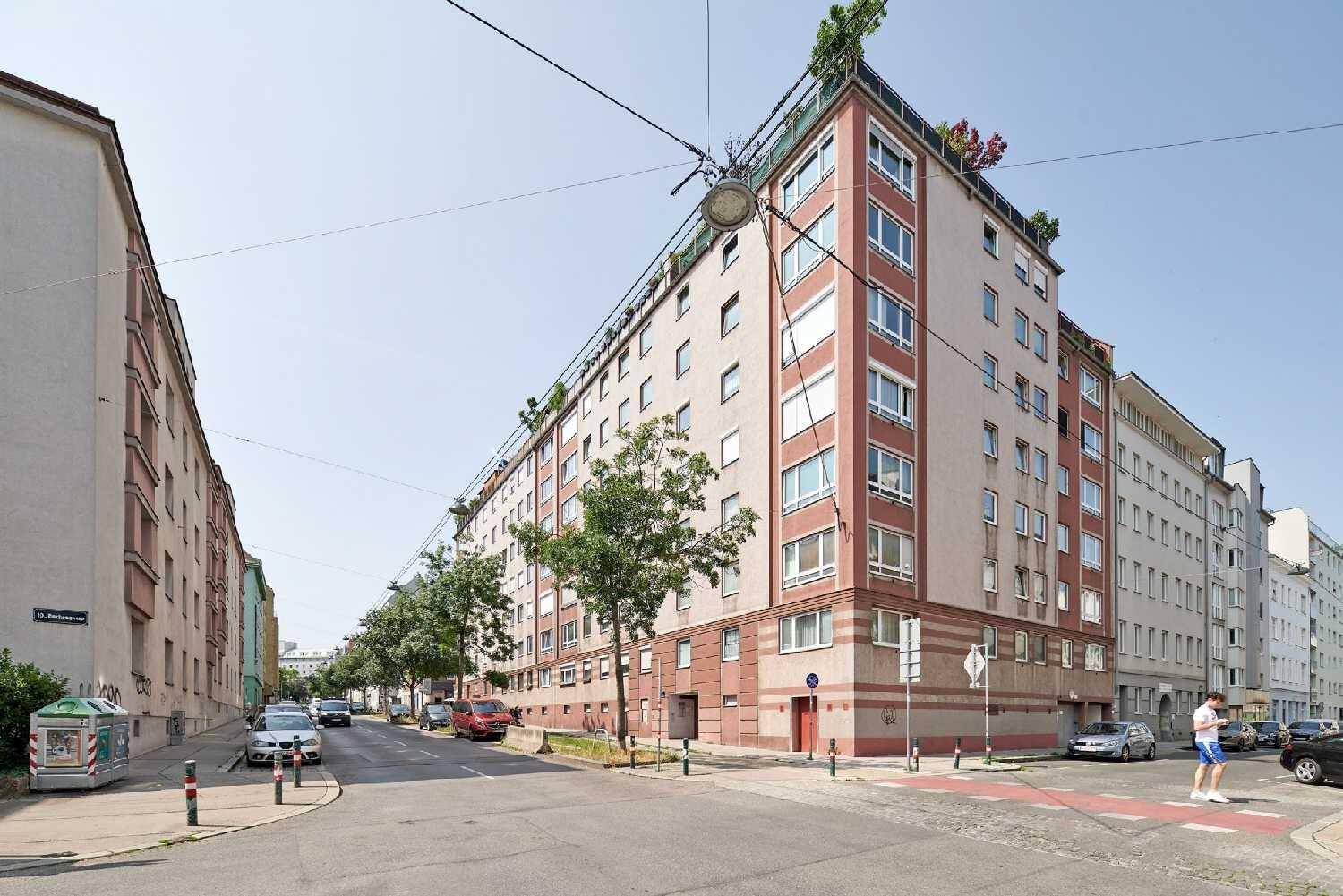Mehrstöckiges Wohngebäude mit roter Fassade und begrüntem Dach in städtischer Umgebung.
