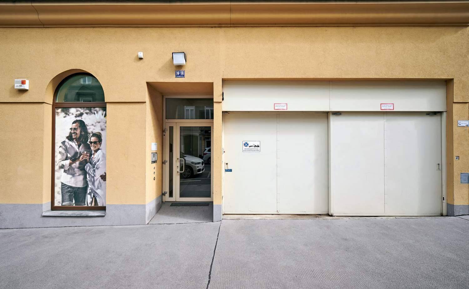 Gebäudeeingang mit Schaufenster und großen Garagentoren an einer städtischen Straße.