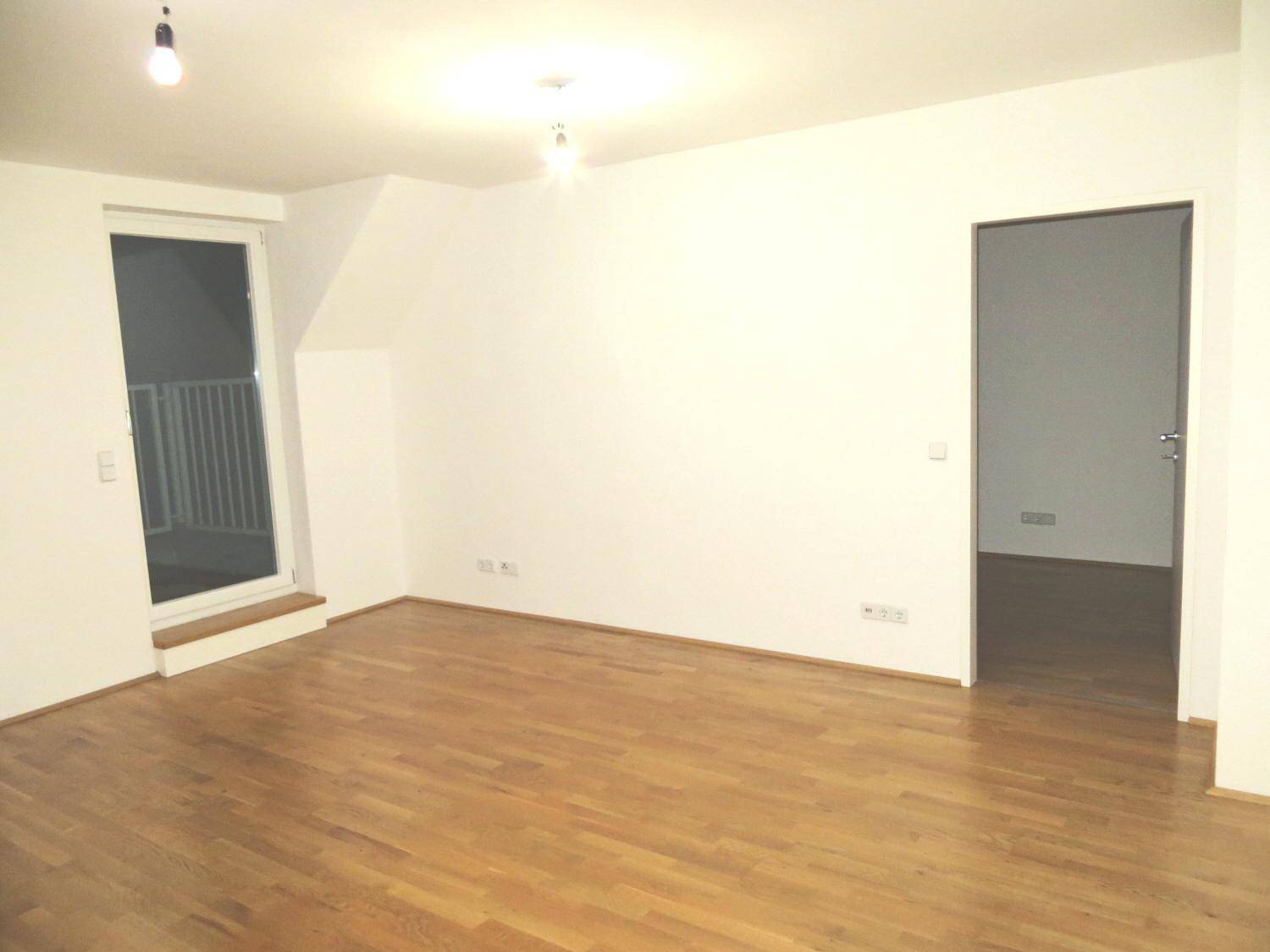 Geräumiger Wohnraum mit Holzboden, Dachschrägen und Zugang zu einem Balkon.